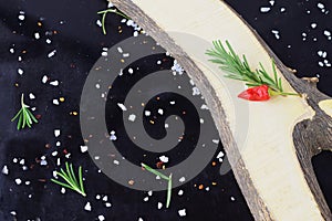 Spices and herbs on a black background with wooden element aside.