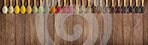 Spices and herbs on wooden table as background for design of packing with food. Collection of spices in spoons with empty space