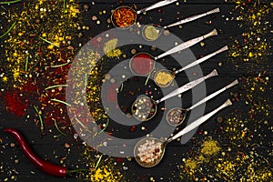 Spices in iron spoons, on a black wooden background