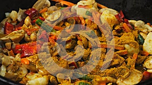 Spices are poured into vegetables and mushrooms fried in a pan.