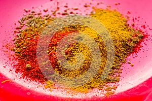 Spices - red pepper, ground coriander, salt and turmeric on a red plate, close-up