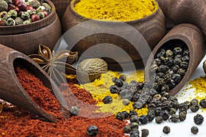 Spices in a wooden bowl and scattered spices on a white background