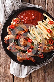 Spicy BBQ chicken wings with french fries and sauce close-up. Vertical top view