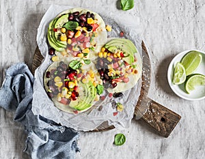 Spicy bean tostadas with corn salsa and avocado on a light background, top view.