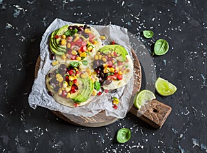 Spicy bean tostadas with corn salsa and avocado on a rustic cutting board on a dark background.