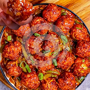 Spicy beef balls, seasoning seeping into them, served with sliced ??lower leaves, topped with chili sauce and thick gravy