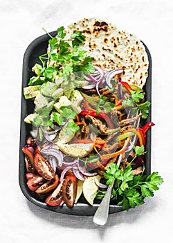 Spicy beef, vegetables, avocado, corn tortillas fajitas on a sheet pan on a light background, top view. Delicious snack, tapas in