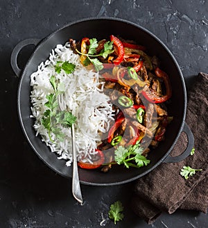 Spicy beef with vegetables and rice in a cast iron skillet on a dark background, top view