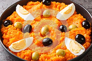 Spicy carrot puree served with boiled eggs and olives close-up in a bowl. horizontal