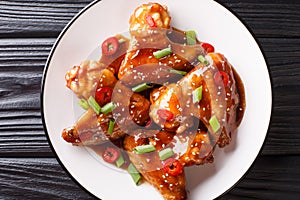 Spicy chicken wings in teriyaki sauce served with green onions and chili pepper close-up on a plate. horizontal top view