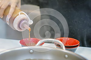 Spicy Chili Sauce Drips out of a Squeeze Bottle into a Bowl at a Shabu-shabu Table