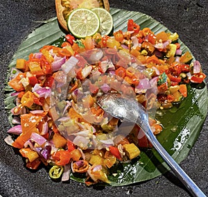 Spicy condiment of Indonesian sambal dabu dabu made of chilli, tomato and shallot with lemon basil in a ceramic bowl, wooden spoon