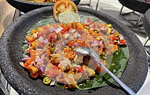 Spicy condiment of Indonesian sambal dabu dabu made of chilli, tomato and shallot with lemon basil in a ceramic bowl, wooden spoon