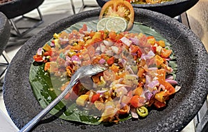 Spicy condiment of Indonesian sambal dabu dabu made of chilli, tomato and shallot with lemon basil in a ceramic bowl, wooden spoon