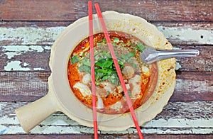 Spicy fish noodle in the bowl with chopsticks and spoon on wood table