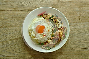 Spicy fried seafood and meat chili and herb on rice topping egg in plate