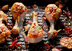 Spicy grilled chicken legs, drumsticks with the addition of chili peppers, garlic and herbs on the grill plate, top view.