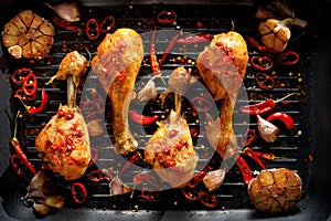 Spicy grilled chicken legs, drumsticks with the addition of chili peppers, garlic and herbs on the grill plate, top view.