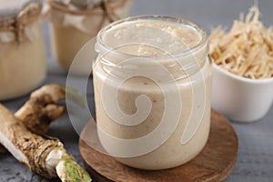 Spicy horseradish sauce in jar and roots on table, closeup