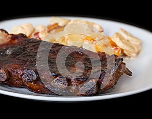 Spicy hot grilled spare ribs from BBQ served on a plate with paprika scalloped potatoes.