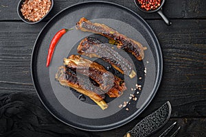 Spicy hot grilled spare ribs from a summer BBQ, on plate, on black wooden table background, top view flat lay