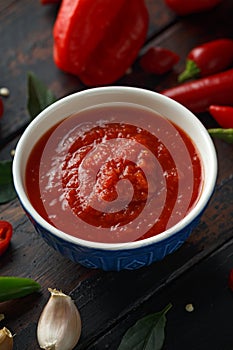 Spicy hot sweet chili sauce with mix of chilli pepper, garlic and tomatoes on rustic wooden background