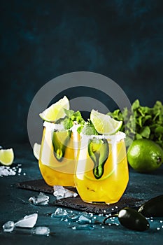 Spicy margarita cocktail with tequila, mango juice, jalapeno pepper, lime and salt, blue background, copy space