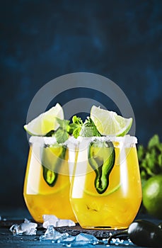 Spicy margarita cocktail with tequila, mango juice, jalapeno pepper, lime and salt, blue background, copy space