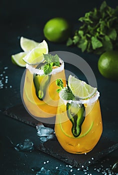 Spicy margarita cocktail with tequila, mango juice, jalapeno pepper, lime and salt, blue background, copy space