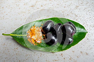 Spicy mixed salt with some black java plum fruit in the green leaves. A way to eat ripe cesium camini fruit by hand. 4k closeup