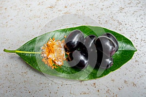 Spicy mixed salt with some black java plum fruit in the green leaves. A way to eat ripe cesium camini fruit by hand. 4k closeup