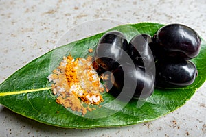 Spicy mixed salt with some black java plum fruit in the green leaves. A way to eat ripe cesium camini fruit by hand. 4k closeup