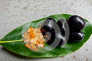 Spicy mixed salt with some black java plum fruit in the green leaves. A way to eat ripe cesium camini fruit by hand. 4k closeup