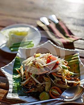 The Spicy papaya salad called `Somtum` in Thai on wooden table with sun light