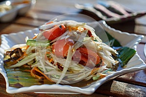 The Spicy papaya salad called `Somtum` in Thai on wooden table with sun light