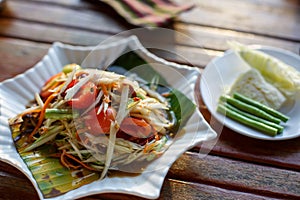 The Spicy papaya salad called `Somtum` in Thai on wooden table with sun light