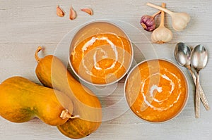 Spicy pumpkin soup with sour cream in the gray bowls decorated with sliced yellow pumpkin on the gray concrete background