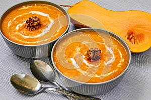 Spicy pumpkin soup with walnuts decorated with sliced yellow pumpkin on the gray concrete background. Traditional autumn food