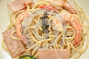 Spicy stir fried spaghetti shrimp with slice ham pork and basil leaf on plate