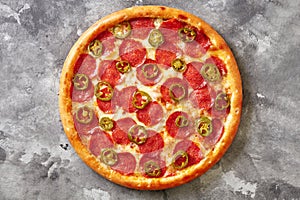 Spicy thin pizza with melted mozzarella, pepperoni and jalapeno on gray stone background