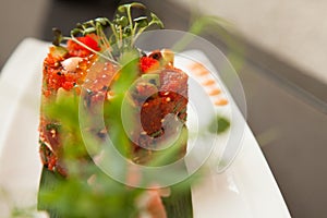 Spicy tuna tartar with Manchuria fish eggs, avocado and sesame seeds served on a long plate viewed trough green leaves