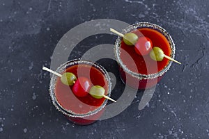 Spicy Vodka Bloody Mary cocktails served with pickled veggies tomatos, olive and celery on a dark background