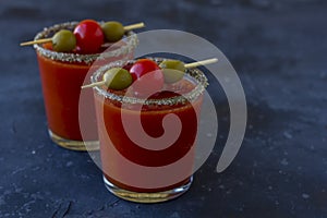 Spicy Vodka Bloody Mary cocktails served with pickled veggies tomatos, olive and celery on a dark background