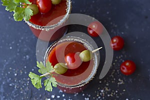 Spicy Vodka Bloody Mary cocktails served with pickled veggies tomatos, olive and celery on a dark background