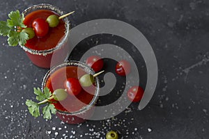 Spicy Vodka Bloody Mary cocktails served with pickled veggies tomatos, olive and celery on a dark background. Close up