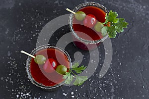Spicy Vodka Bloody Mary cocktails served with pickled veggies tomatos, olive and celery on a dark background. Close up, copy