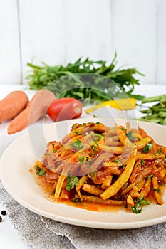 Spicy warm salad of green beans in tomato sauce on a plate on a white wooden background.