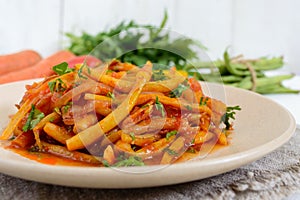 Spicy warm salad of green beans in tomato sauce on a plate on a white wooden background.