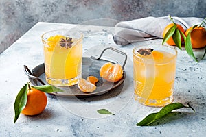 Spicy winter yellow orange cocktail or mocktail with fresh tangerines and anise on grey background.