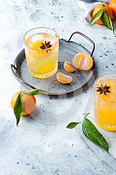 Spicy winter yellow orange cocktail or mocktail with fresh tangerines and anise on grey background.